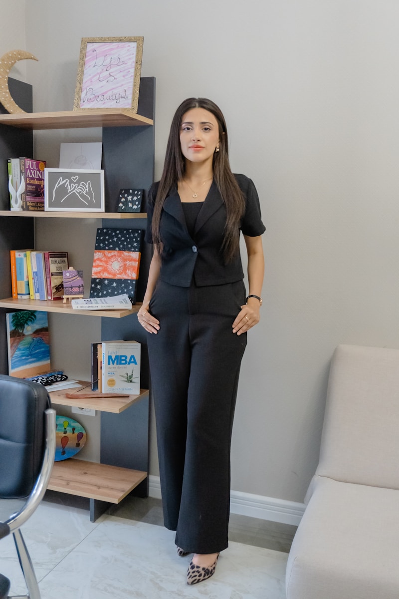 A woman in a black suit stands by a bookshelf.